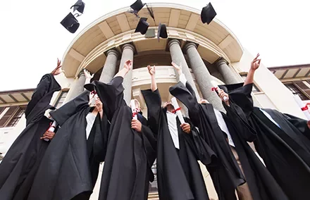 Estudantes jogam seus chapéus de formatura no ar em festa.