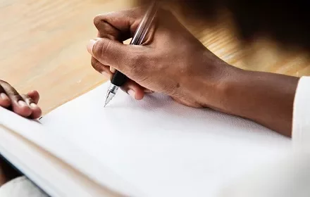Pessoa escrevendo em um caderno com caneta preta.
