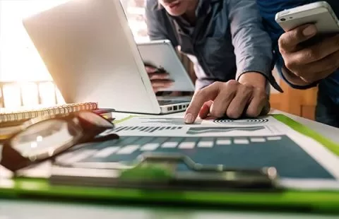 Pessoas trabalhando com laptop e smartphone em mesa de escritório.